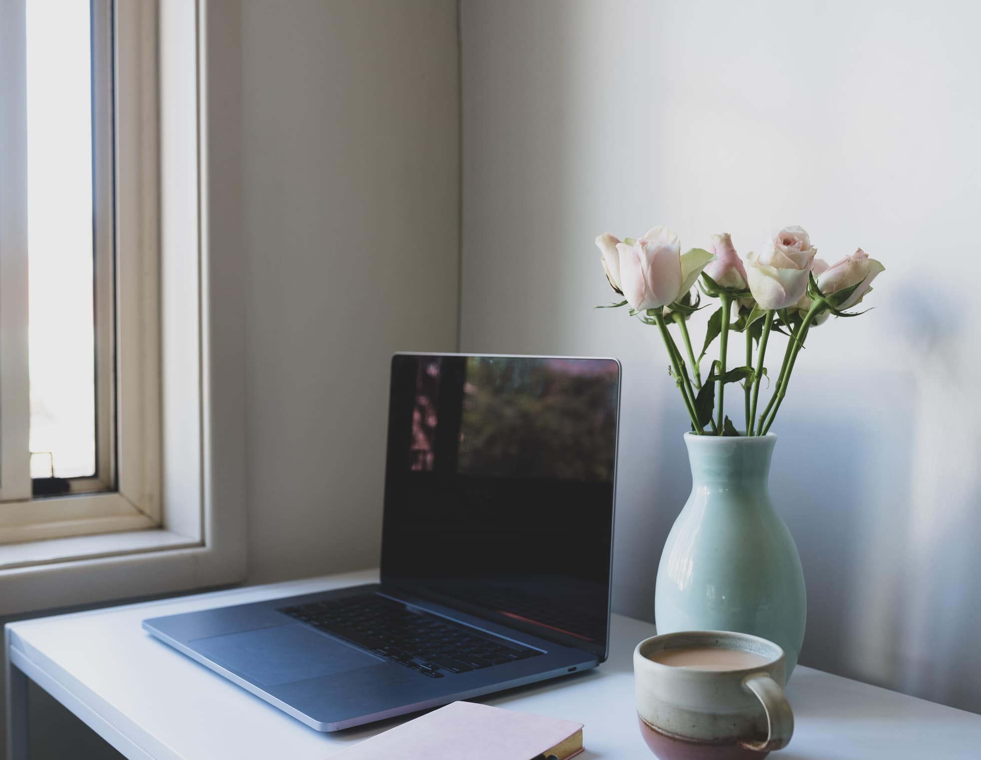 home office desk with laptop and roses in a vase