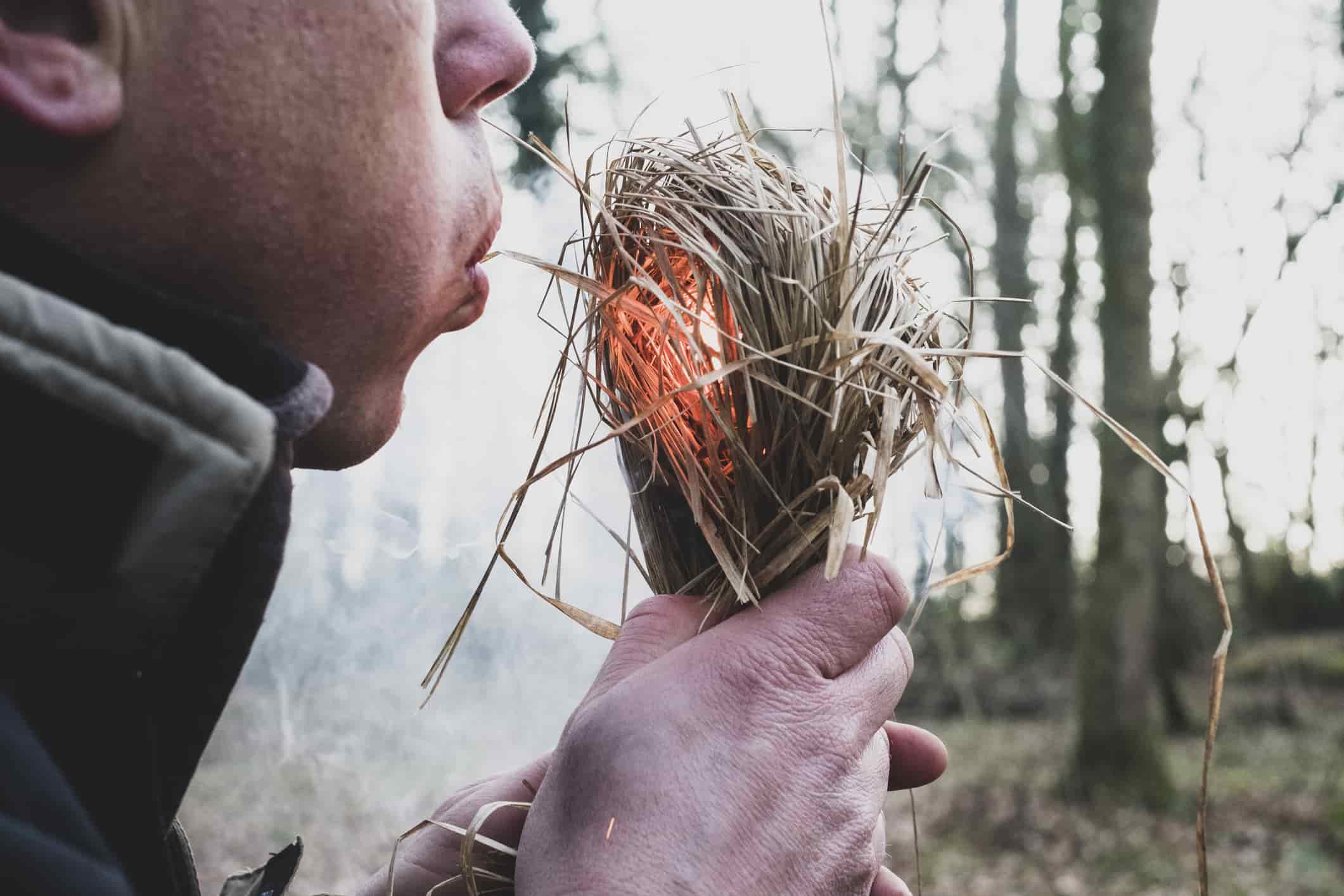 Close up of man blowing on bundle of straw, igniting fire