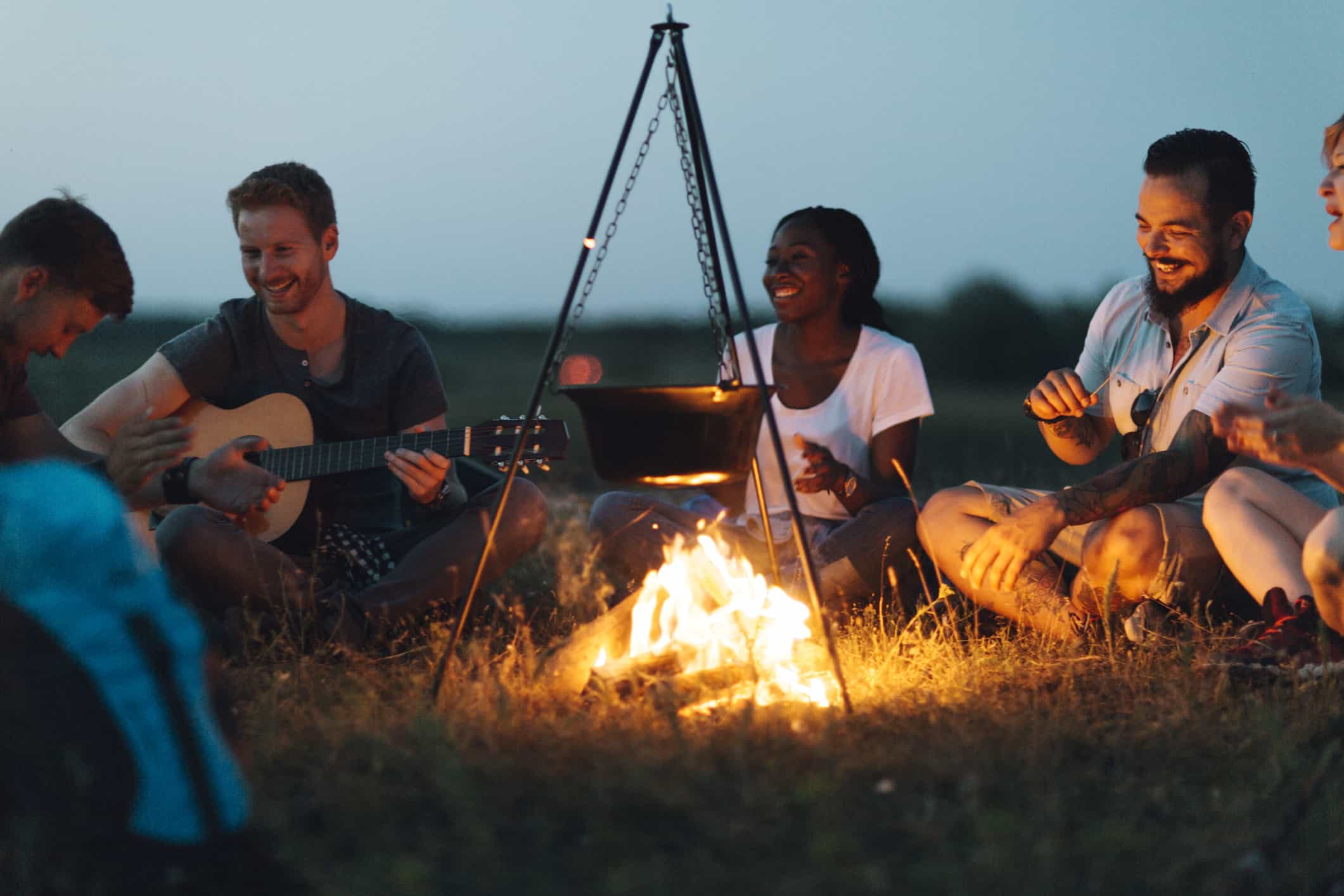 Friends playing music and smiling around the campfire