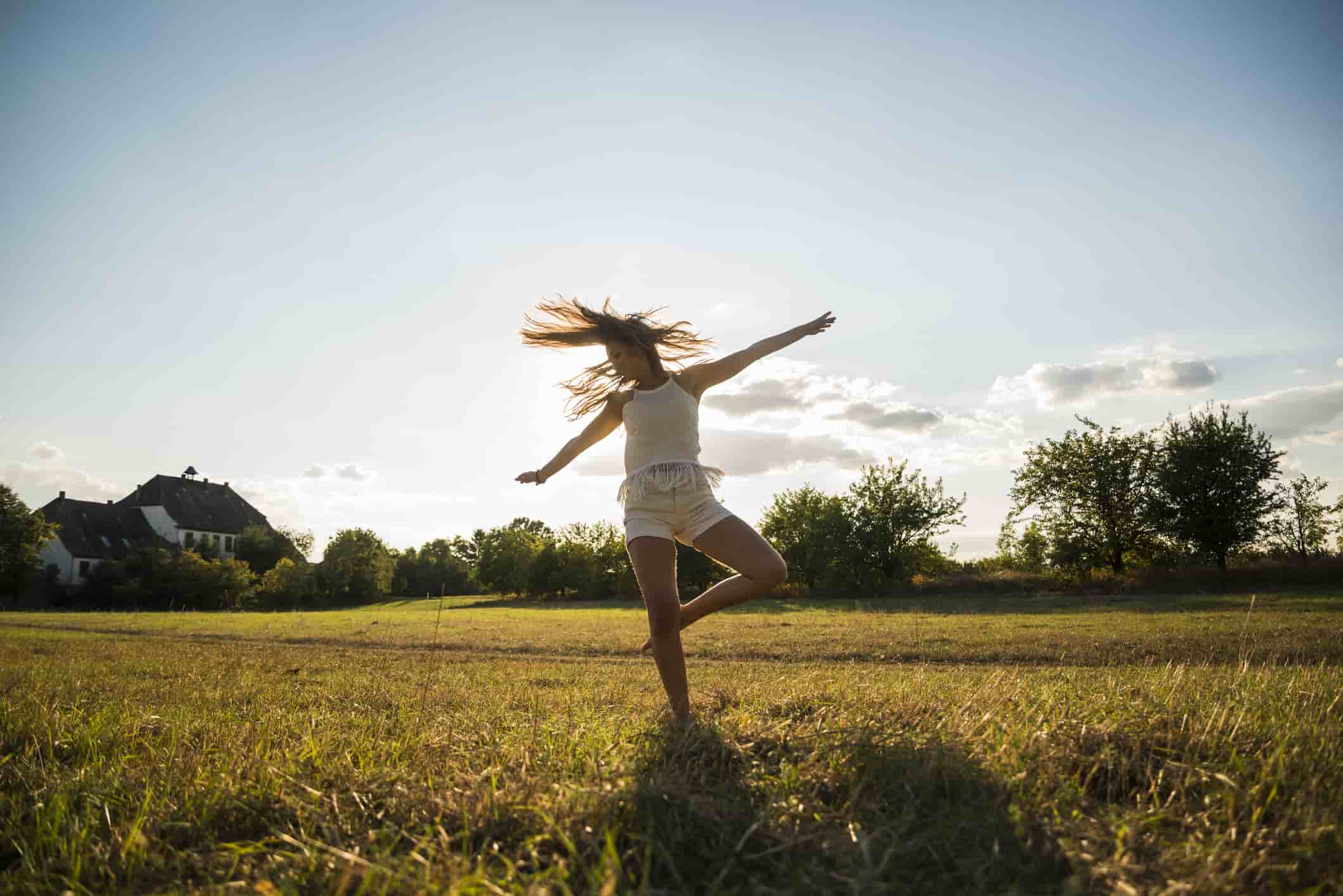 Young woman dancing on a meadow at backlight