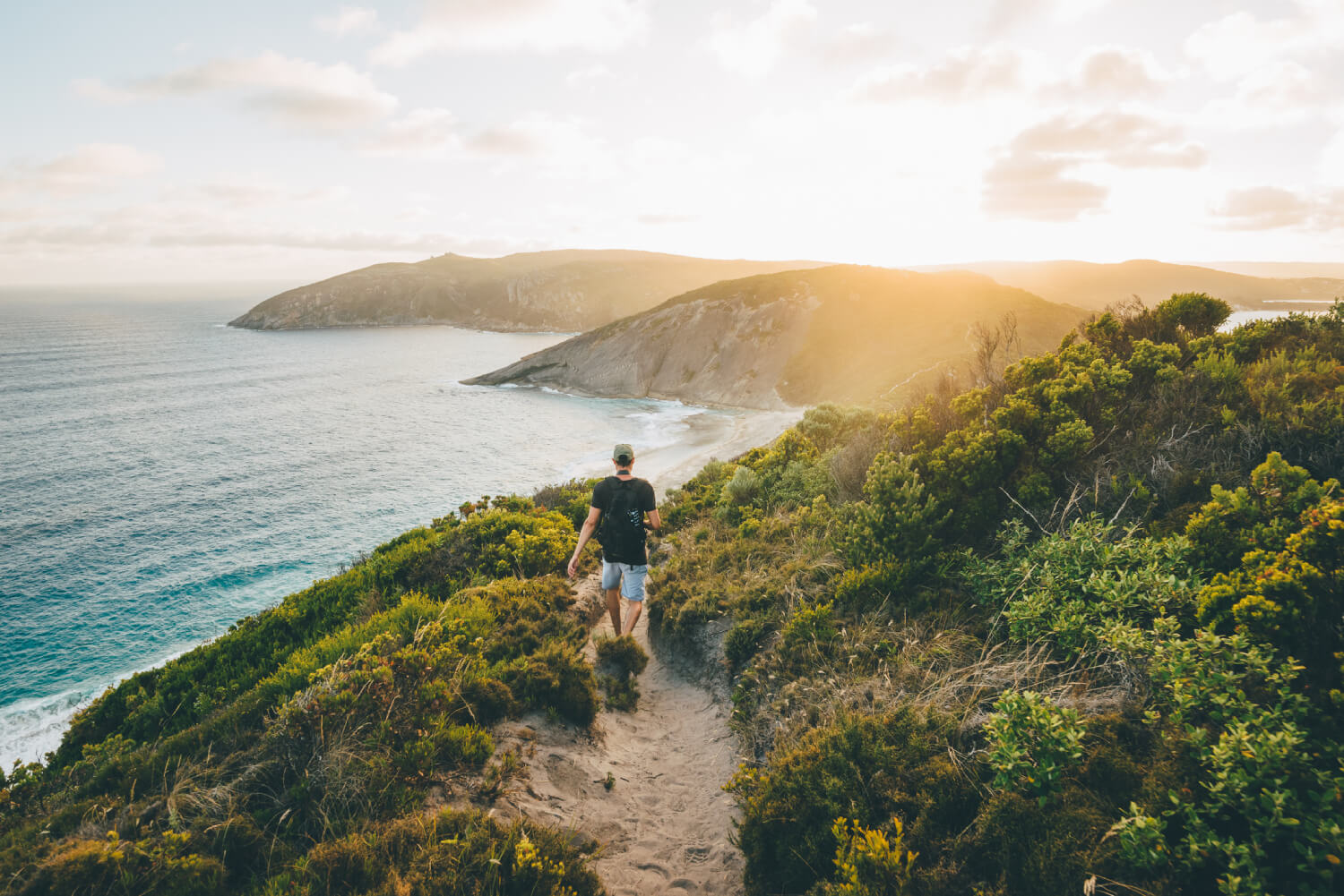 a person walking on a hiking trail near the ocean during the day